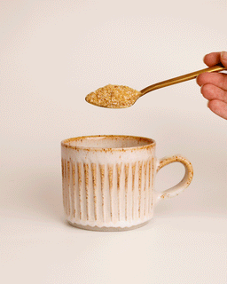 A teaspoon of beef bone broth powder being tipped into a mug of boiling water