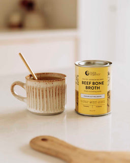 A cup of broth sits next to a tin of Nutra Organic's Beef Bone Broth Turmeric