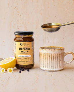 A cup of broth sits next to a jar of Nutra Organic's Beef Bone Broth concentrate lemon ginger ACV