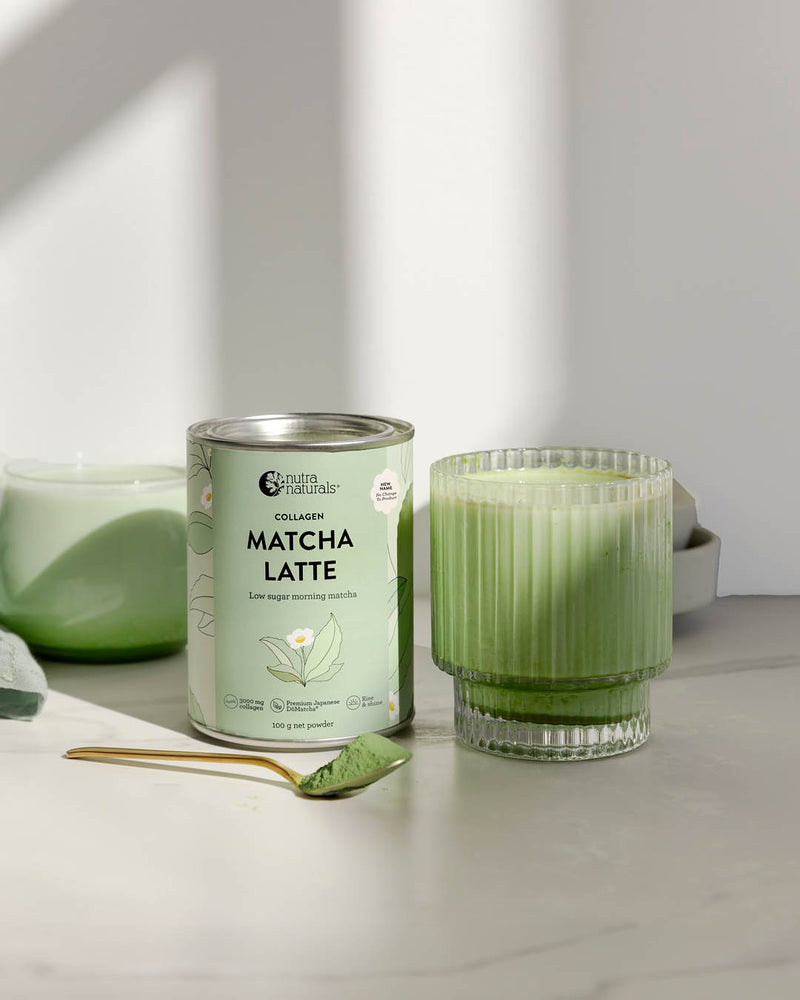 A can of Collagen Matcha Latte powder stands next to a glass of green matcha latte on a light marble surface with soft shadows.