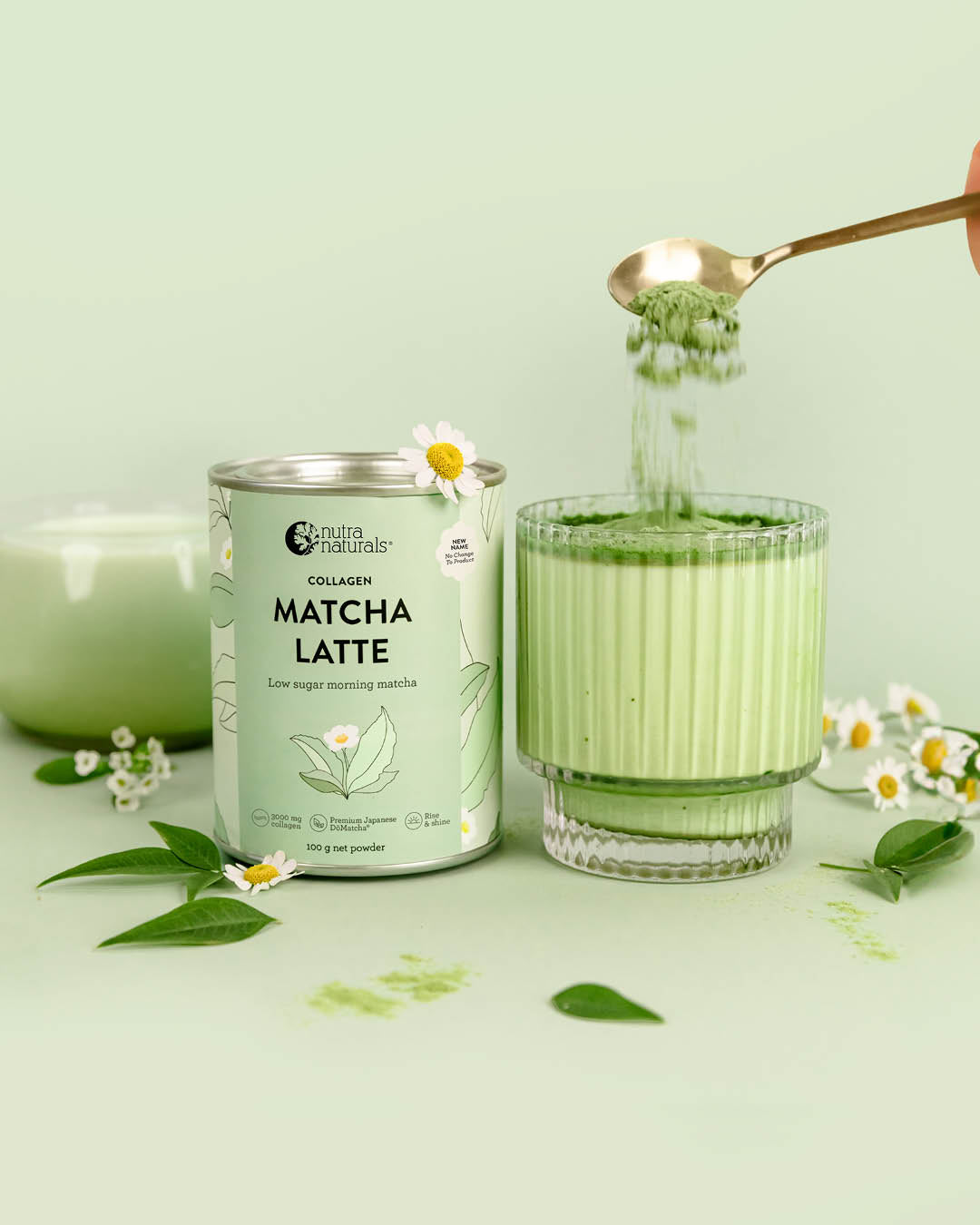 A can of Collagen Matcha Latte powder stands next to a glass of light green latte with matcha powder being poured from a gold spoon.