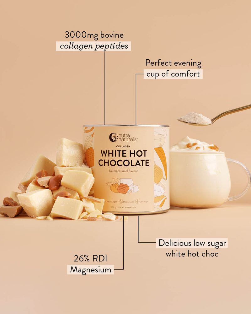 A can of Collagen White Hot Chocolate shown on a warm beige background with callout lines highlighting key selling points: 3000mg bovine collagen peptides, perfect evening cup of comfort, 26% RDI magnesium, and delicious low sugar white hot choc. White chocolate chunks and a cup of white hot chocolate with whipped cream are arranged around the product.