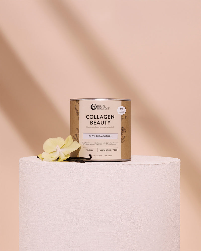 A can of Collagen Beauty styled on a white cylindrical pedestal with a yellow orchid flower and vanilla bean against a soft peach background.