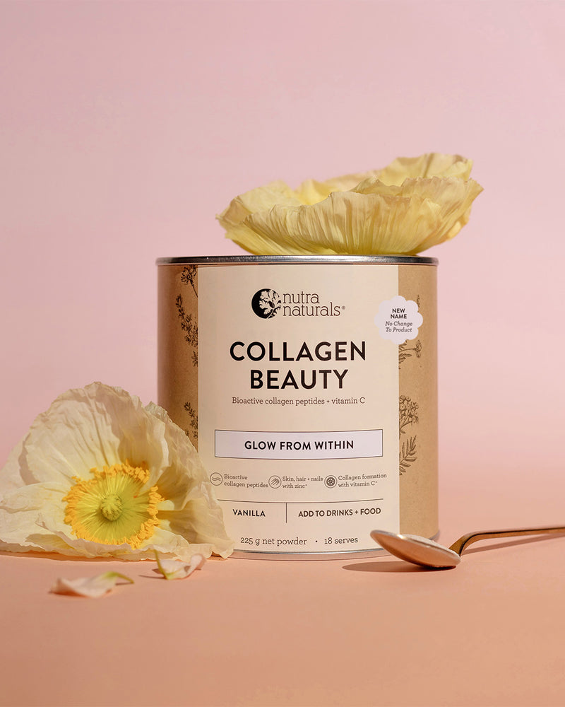 A can of Nutra Naturals Collagen Beauty powder stands on a soft pink background with decorative white flowers and a spoon around it.