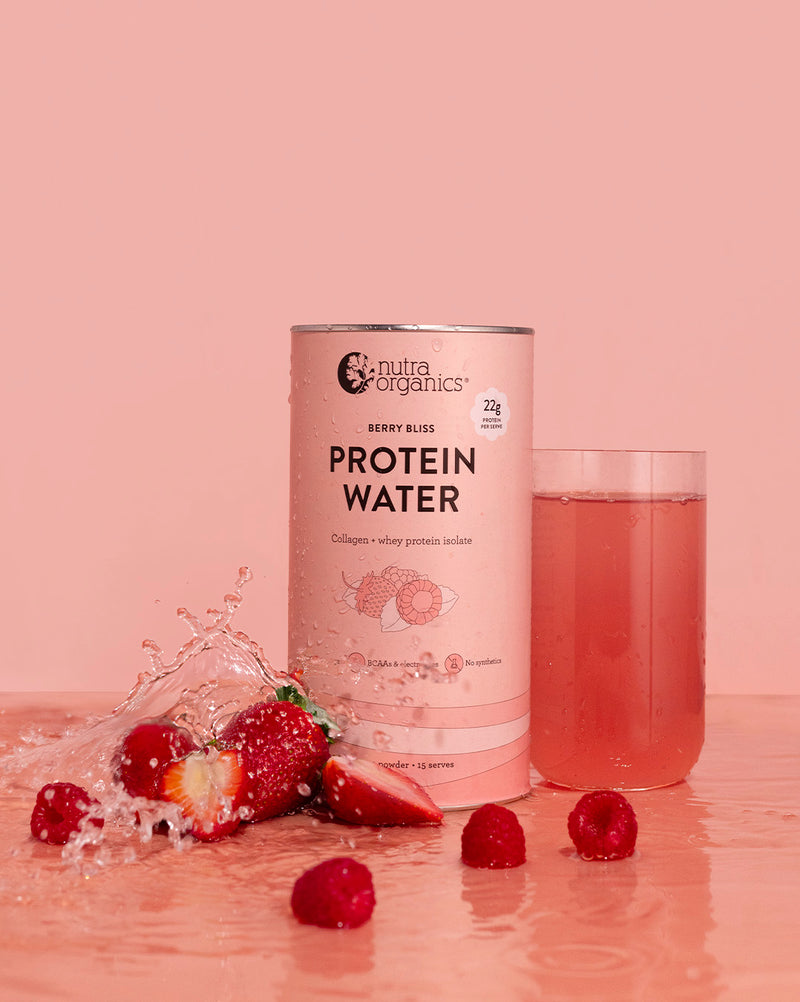Protein Water Berry Bliss canister with a glass of water and berries on a pink background