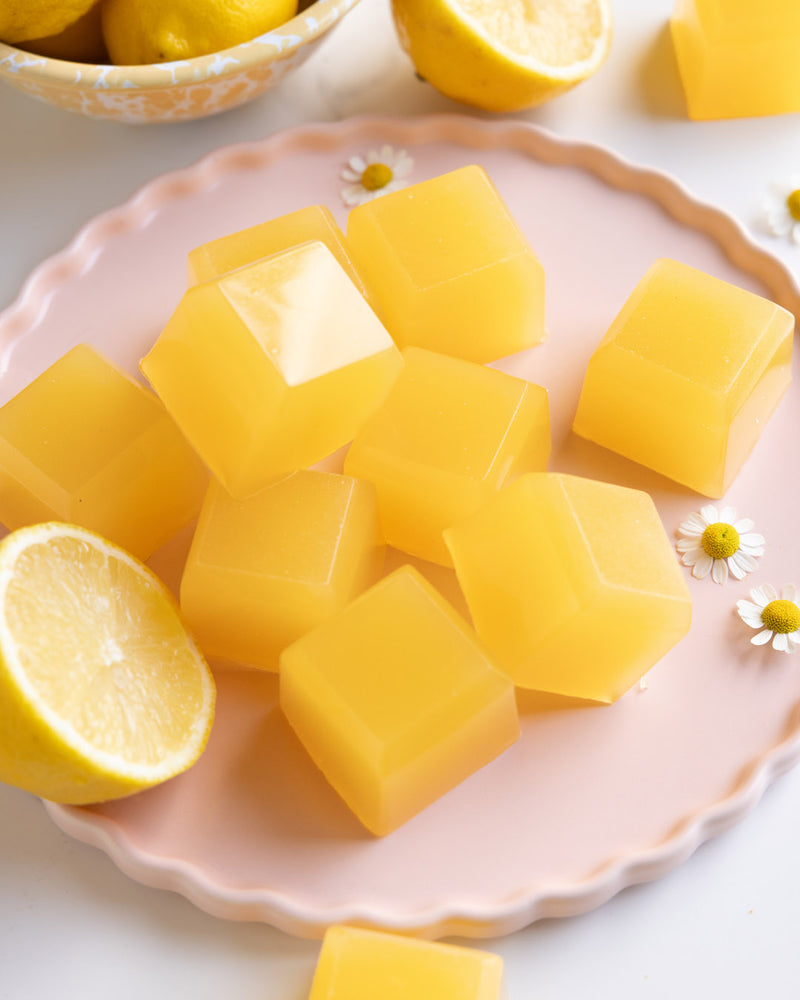 Yellow cubes on a pink plate with lemons and daisies on a white background