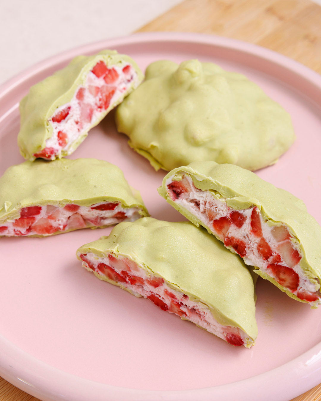Green pastries with strawberry filling on a pink plate