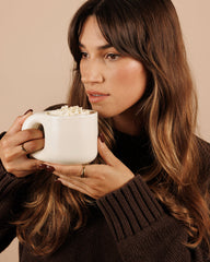 Woman holding a white mug with a warm beverage against a beige background